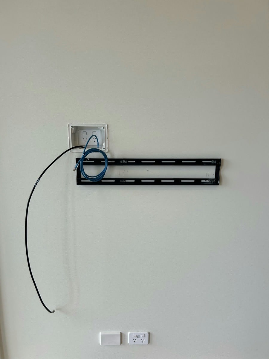 A television bracket fixed to the wall before the screen goes on, with the recessed outlet above and the antenna cable looping to the outlet below
