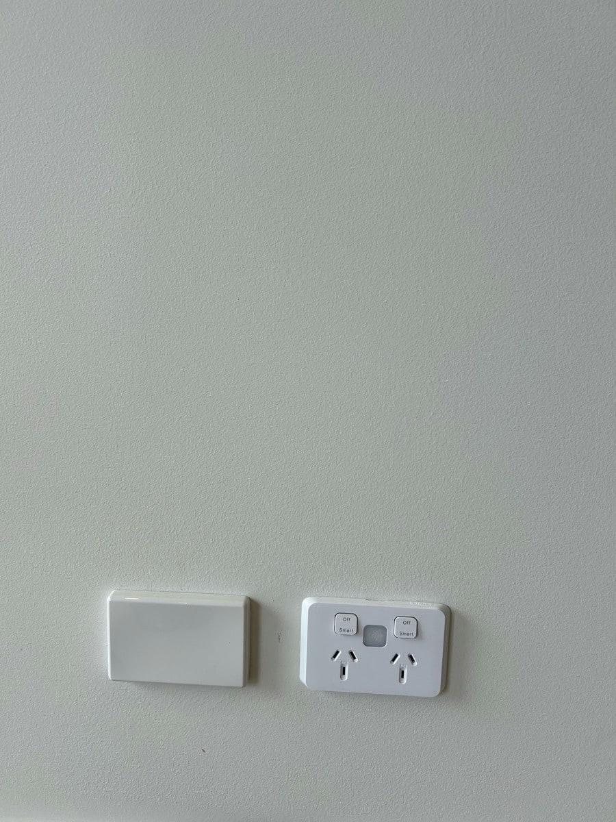 A blank cable entry plate beside a double power point on a plain wall