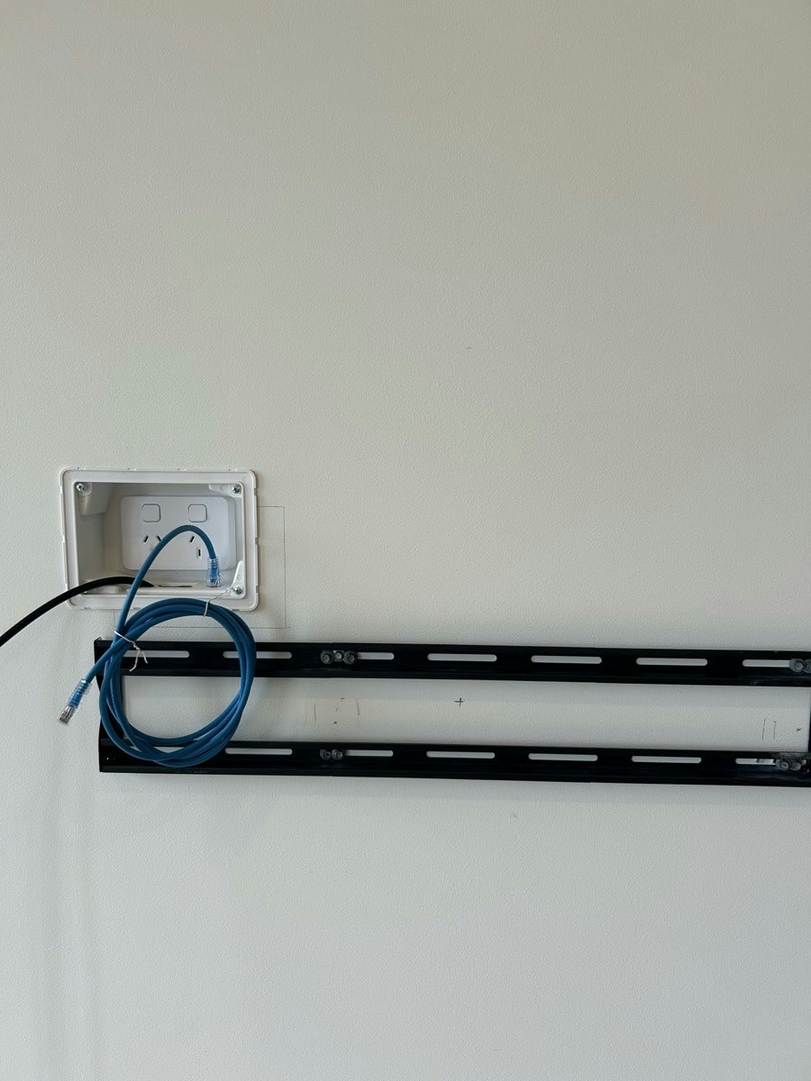 A power point set back inside a recessed box so the plug sits inside the wall, with the data cable coiled beside it
