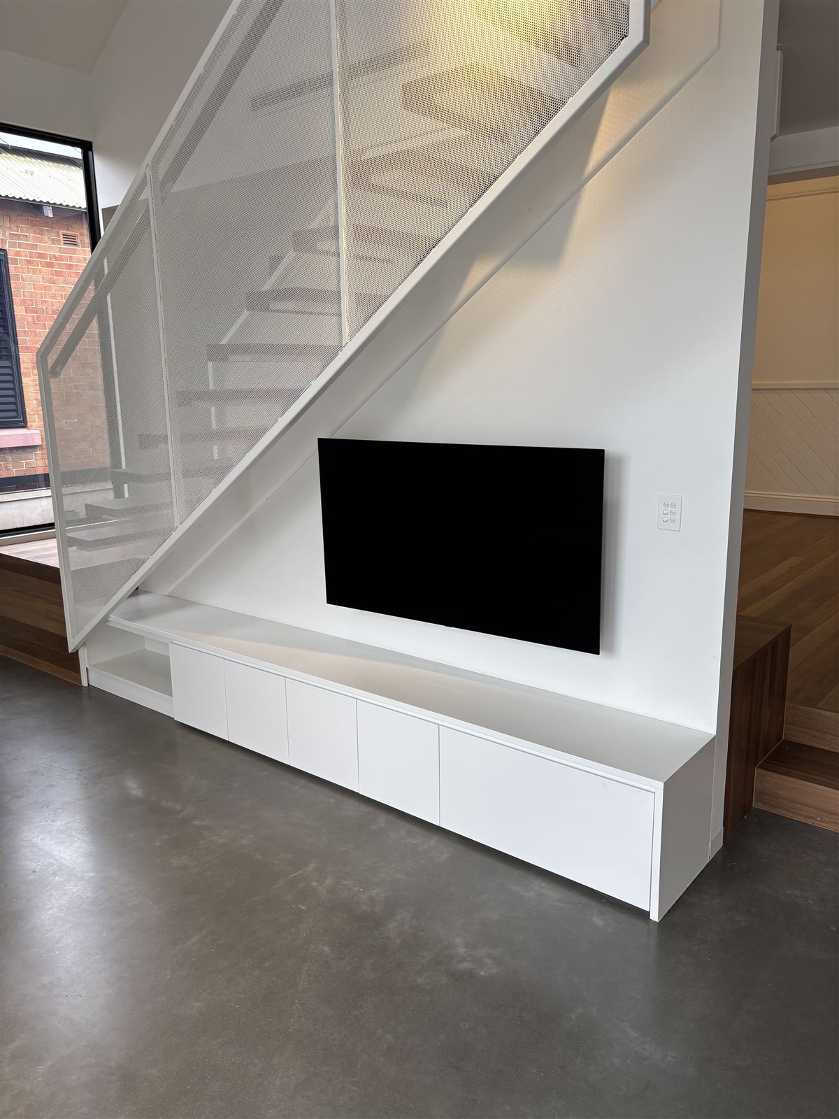 A wall-mounted television under a staircase with no cables showing, joinery beneath it