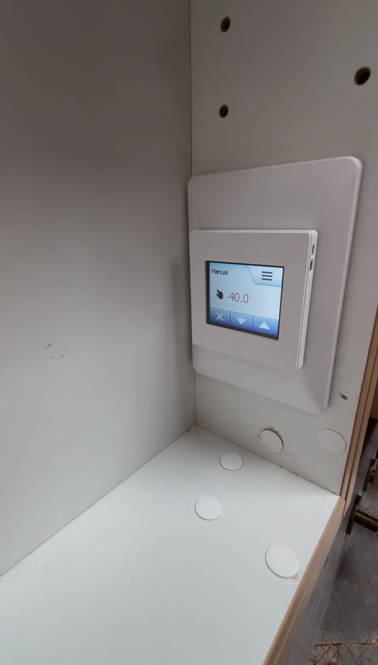 An underfloor heating thermostat fitted in a wall recess with its display on