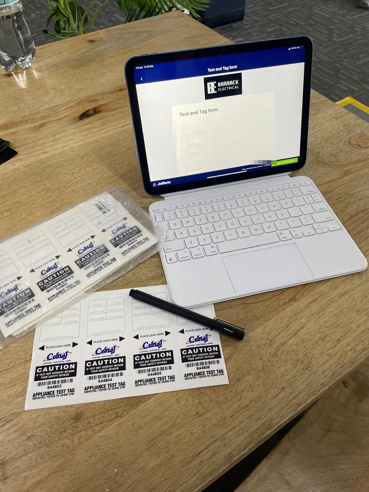 Appliance test tags beside a tablet showing a Barrack Electrical test and tag form